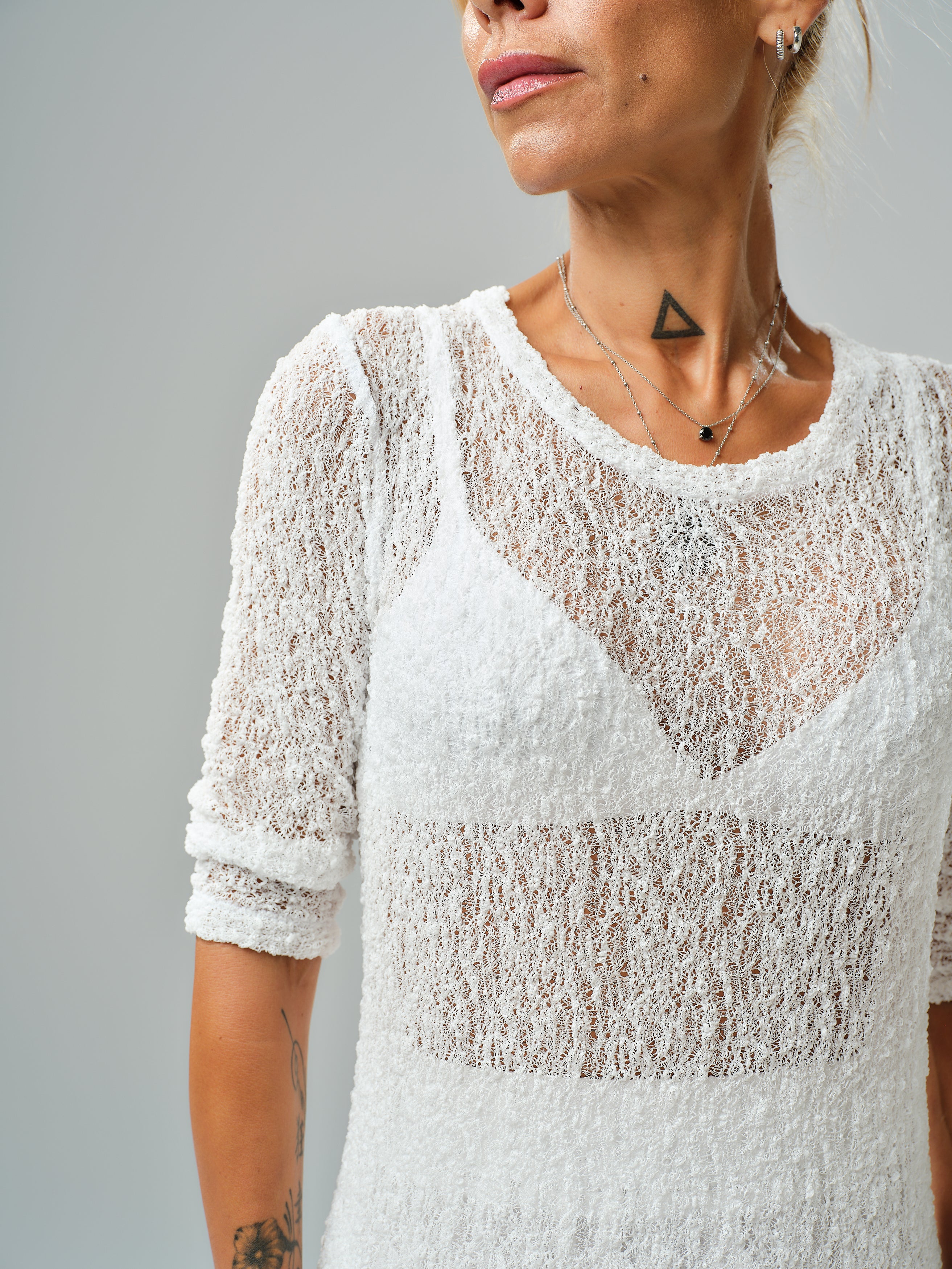 Close-up of a woman wearing a sheer white tunic with textured fabric and a stylish neckline.