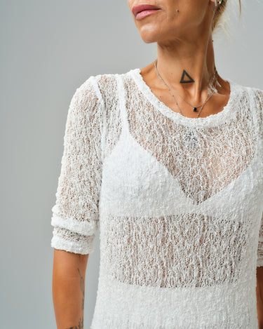 Close-up of a woman wearing a sheer white tunic with textured fabric and a stylish neckline.