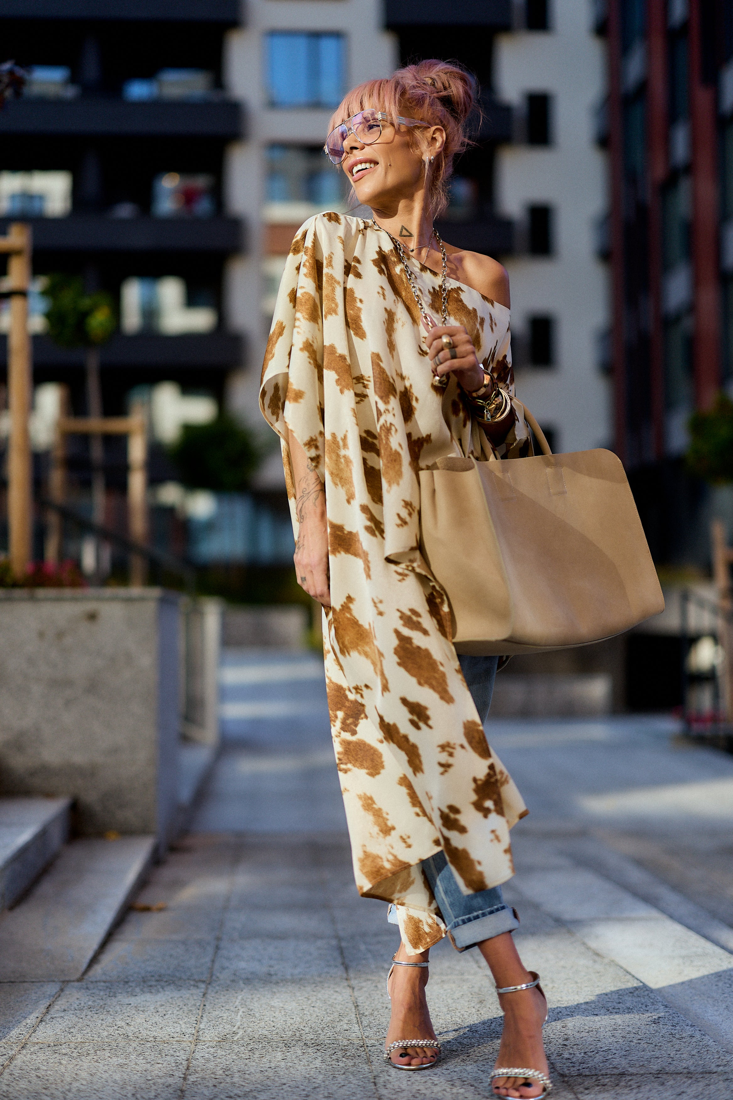 Woman wearing a Beige Printed Asymmetric Tunic with a camel-toned abstract print, styled with jeans and a tote bag.