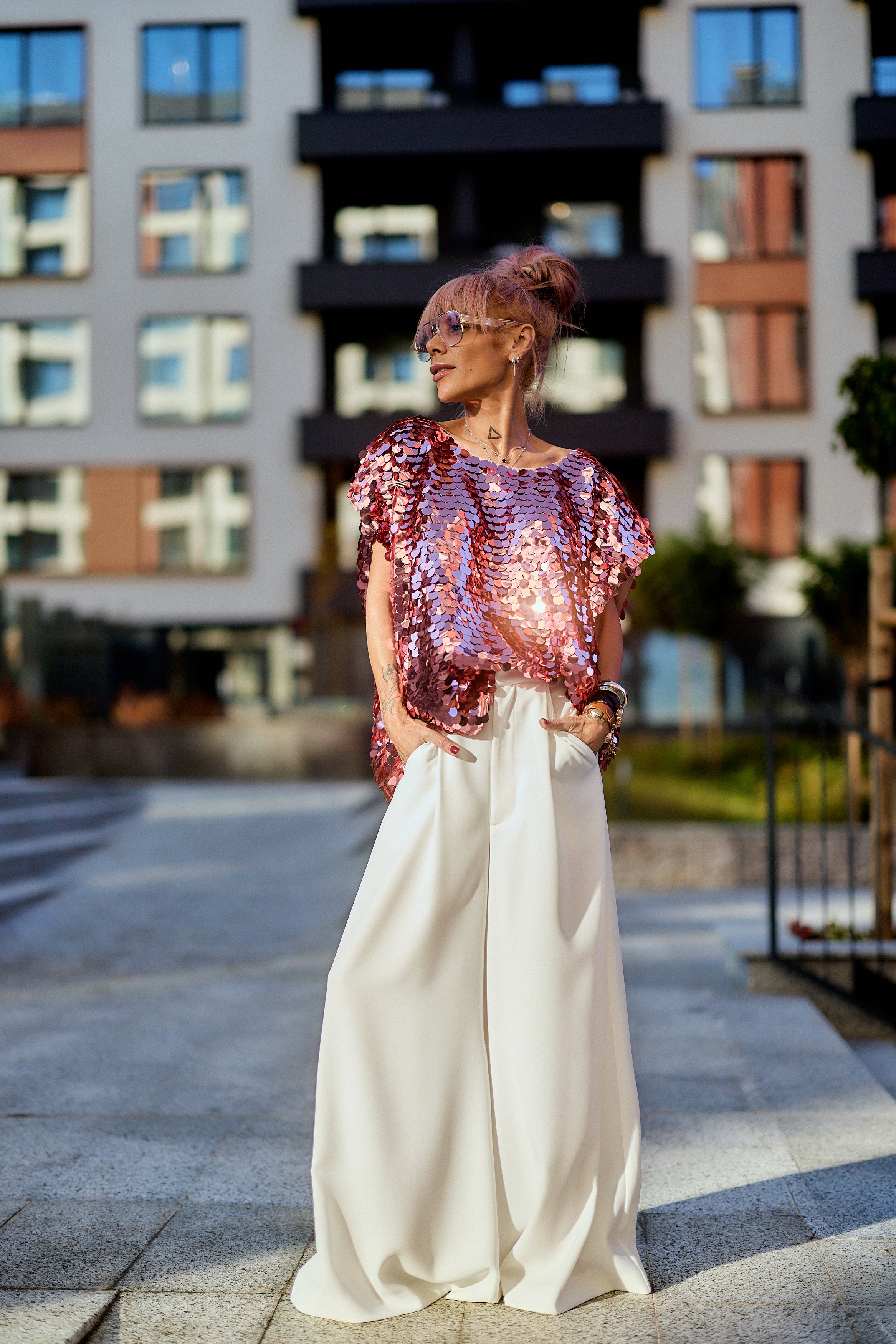Model wearing Pink Sequin Oversized Top with wide pants in urban setting, showcasing modern eveningwear style.