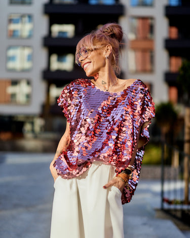 A woman wearing a Pink Sequin Oversized Top with oversized sequins, set against an urban backdrop.