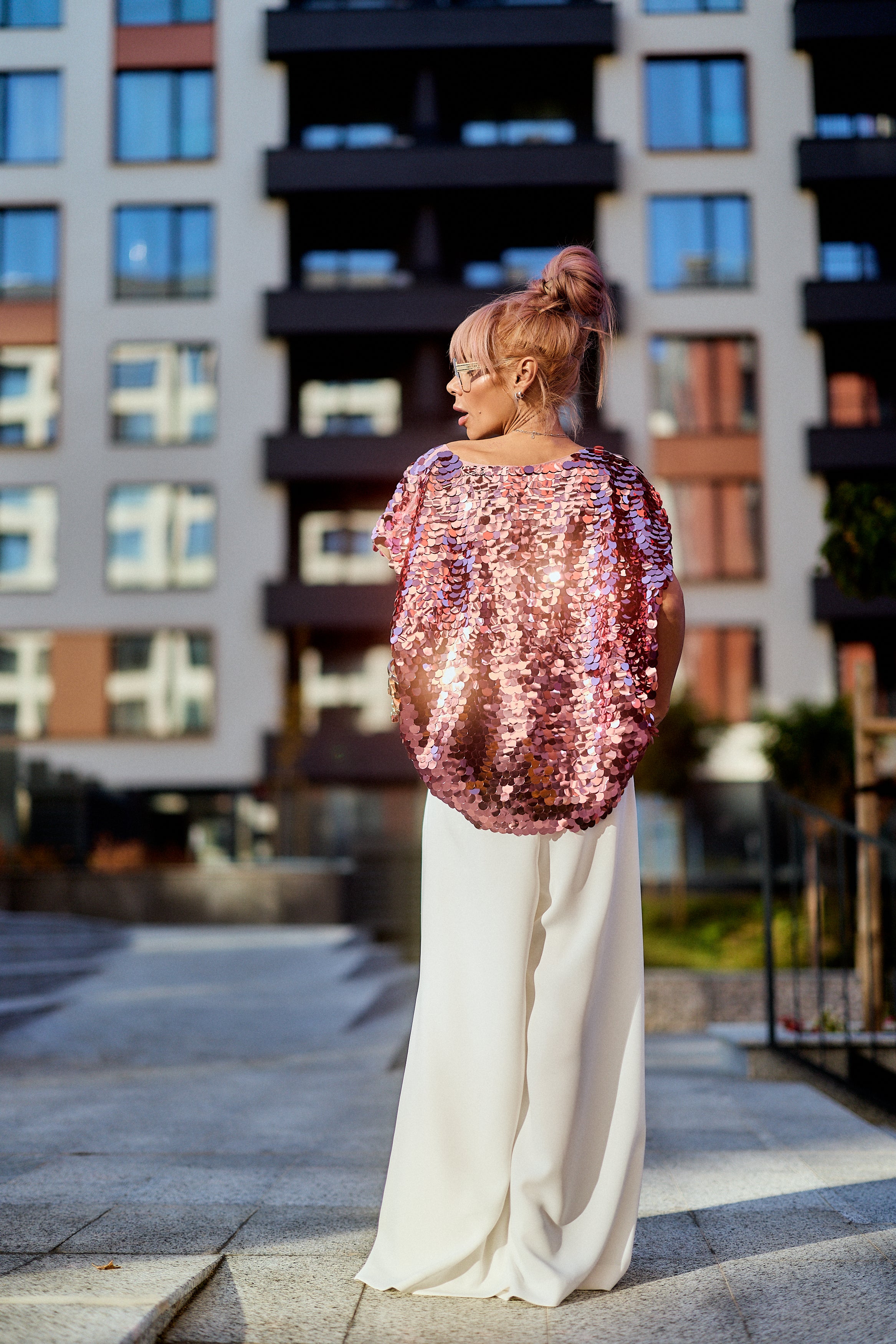 A model showcasing the Pink Sequin Oversized Top in luminous pink tones, paired with wide white trousers.