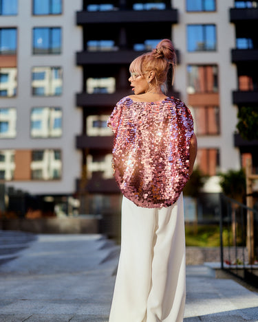 A model showcasing the Pink Sequin Oversized Top in luminous pink tones, paired with wide white trousers.
