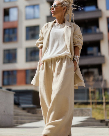 Woman in beige outfit standing in an urban setting with buildings in the background