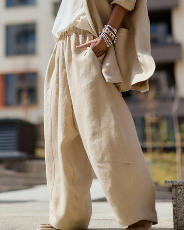 Person wearing a beige outfit standing in an urban setting with buildings in the background