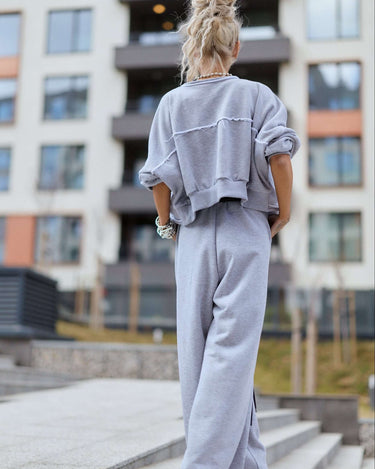 A woman wearing a Grey Relaxed Lounge Set, featuring a cropped top and wide-leg pants, set against a modern building backdrop.