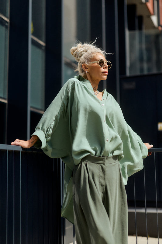 Woman in a green outfit standing against a dark building.