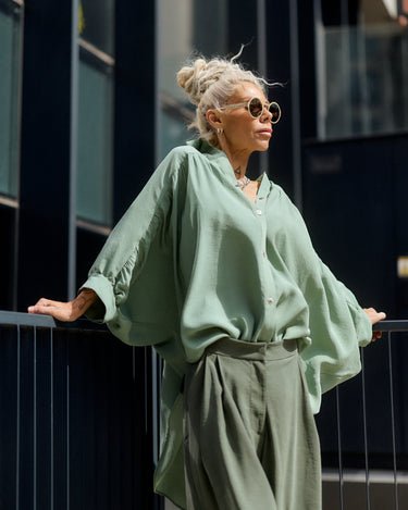 Woman in a green outfit standing against a dark building.