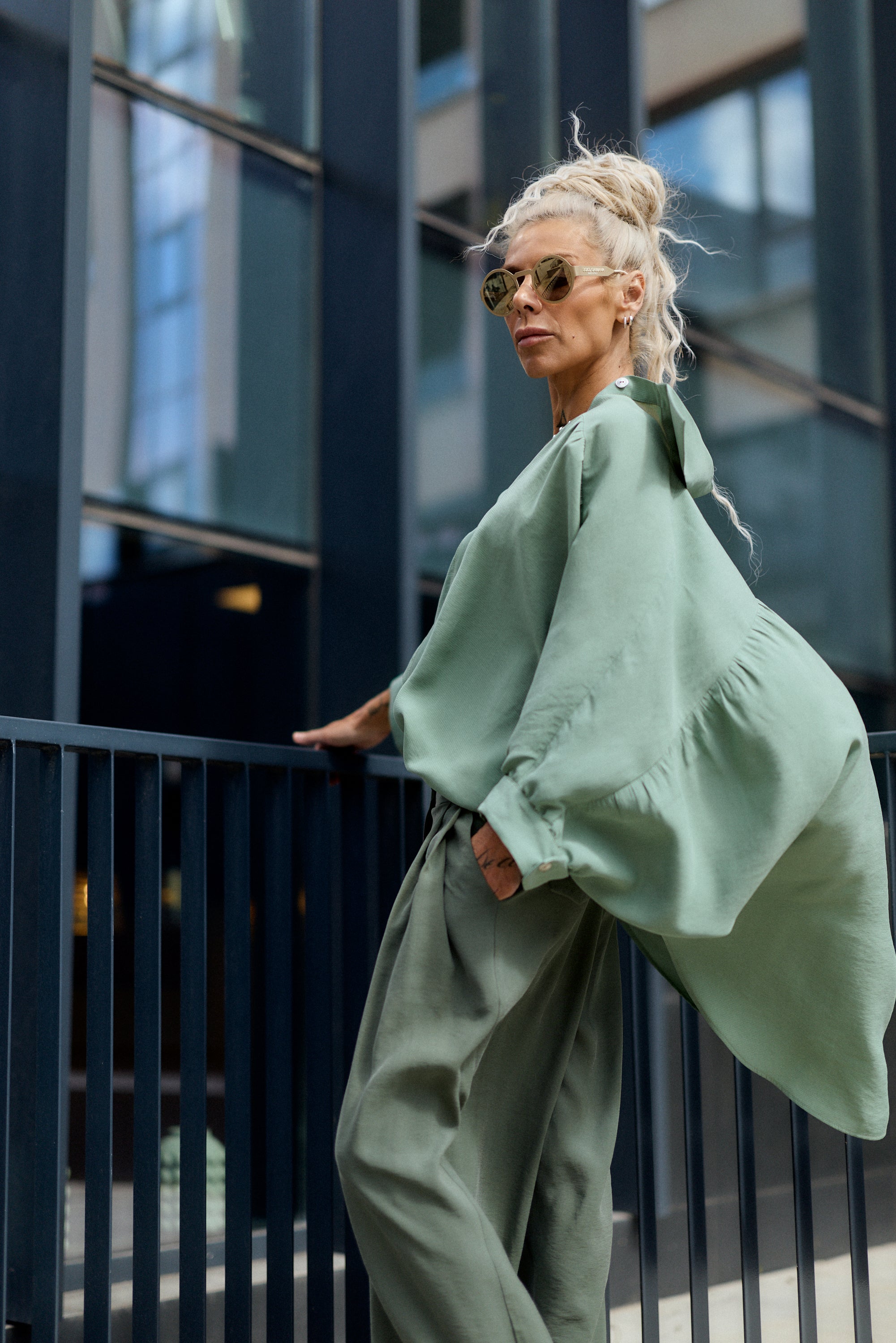 Woman in a green outfit standing against a modern building.