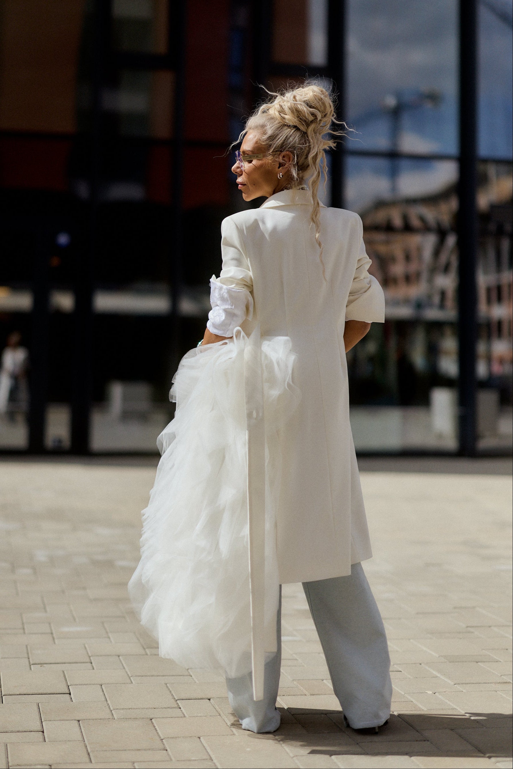 Person in a white outfit with a long coat and high-waisted pants standing on a street.