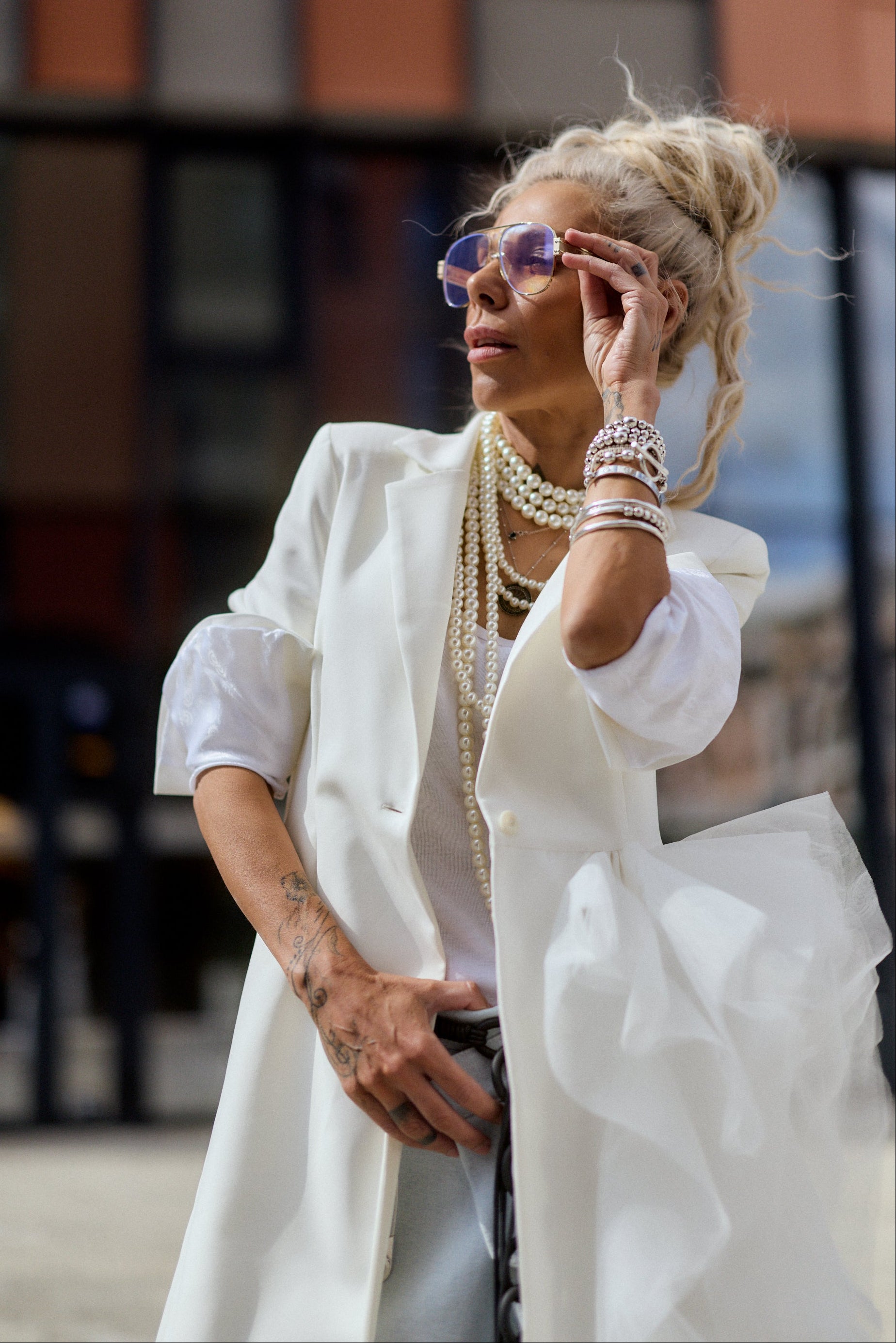 Woman in a white outfit with layered necklaces and sunglasses outdoors.