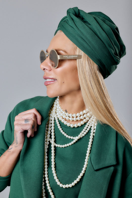 Woman wearing an Emerald Green Turban Hat with oversized sunglasses and layered pearl necklaces.
