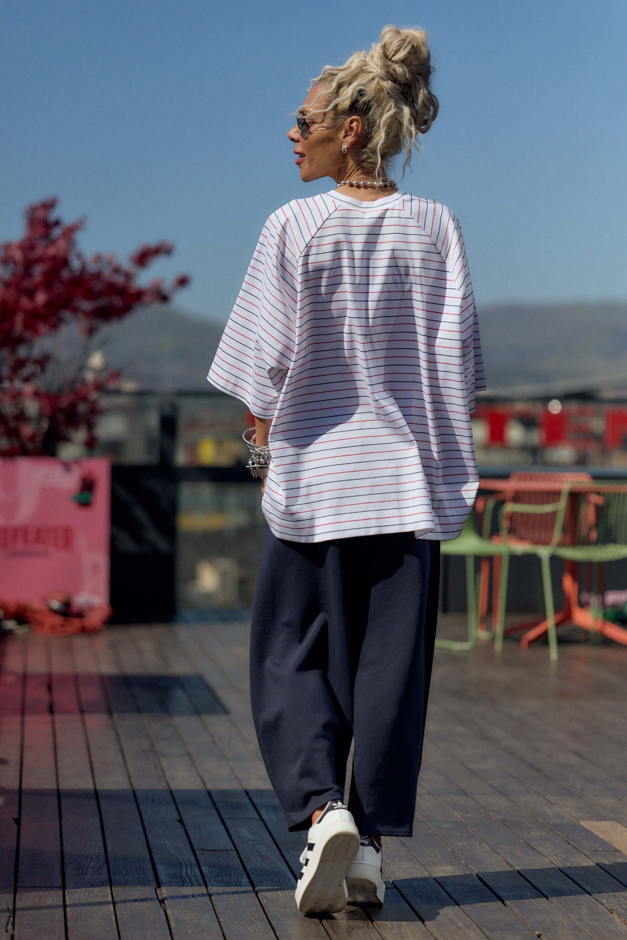 Person wearing a striped shirt and dark pants on a wooden deck with a scenic background