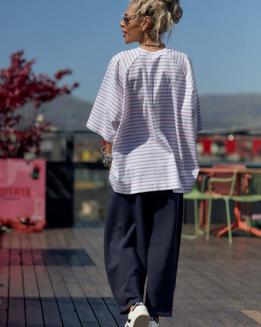 Person wearing a striped shirt and dark pants on a wooden deck with a scenic background