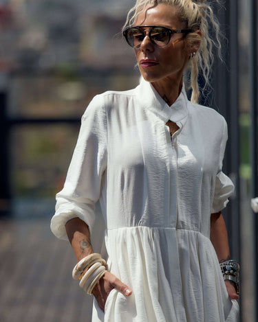 Flowing White Maxi Dress worn by a woman with accessories, showcasing elegance and fluid movement outdoors.