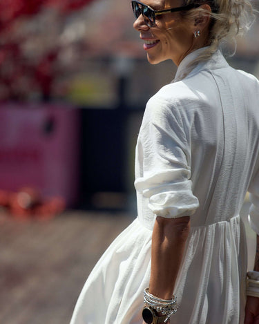 Woman wearing a Flowing White Maxi Dress with a distinctive neckline, enjoying the sunshine outdoors.
