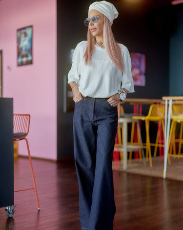 Fashionable woman wearing Wide-Leg Raw Denim Jeans with a stylish blouse and head wrap in a modern setting.
