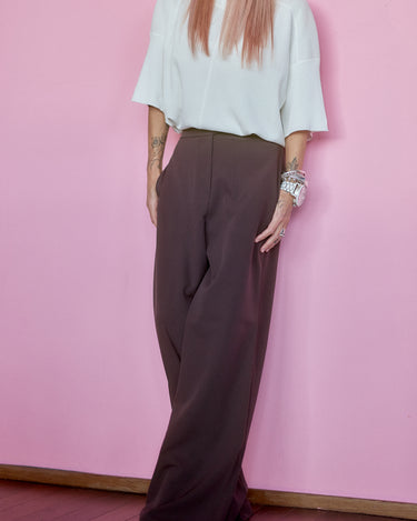 Wide-Leg Tailored Pants in Dark Brown worn with a light top against a pink wall for a stylish look.