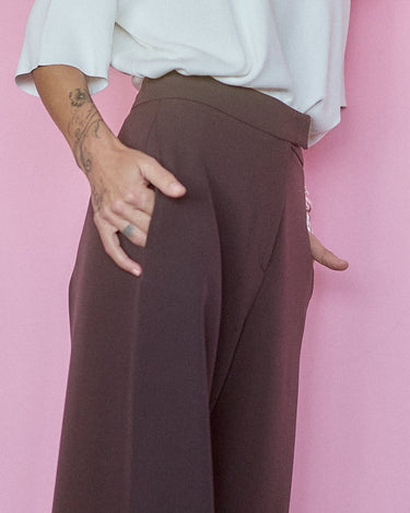 Model showcasing Wide-Leg Tailored Pants in Dark Brown against a pink background, emphasizing comfort and style.