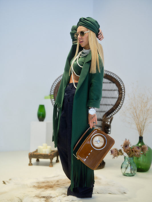 Model wearing a Green Long Coat with Fringe Detail, styled with accessories, showcasing a chic look in a modern setting.