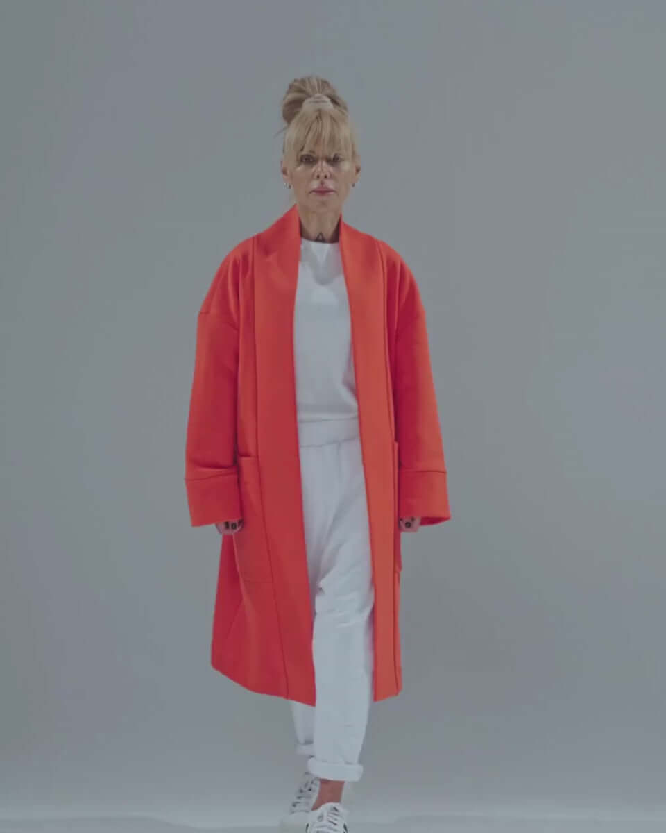 Model wearing a bold red oversized coat over a white outfit, showcasing a minimalist style with casual comfort.