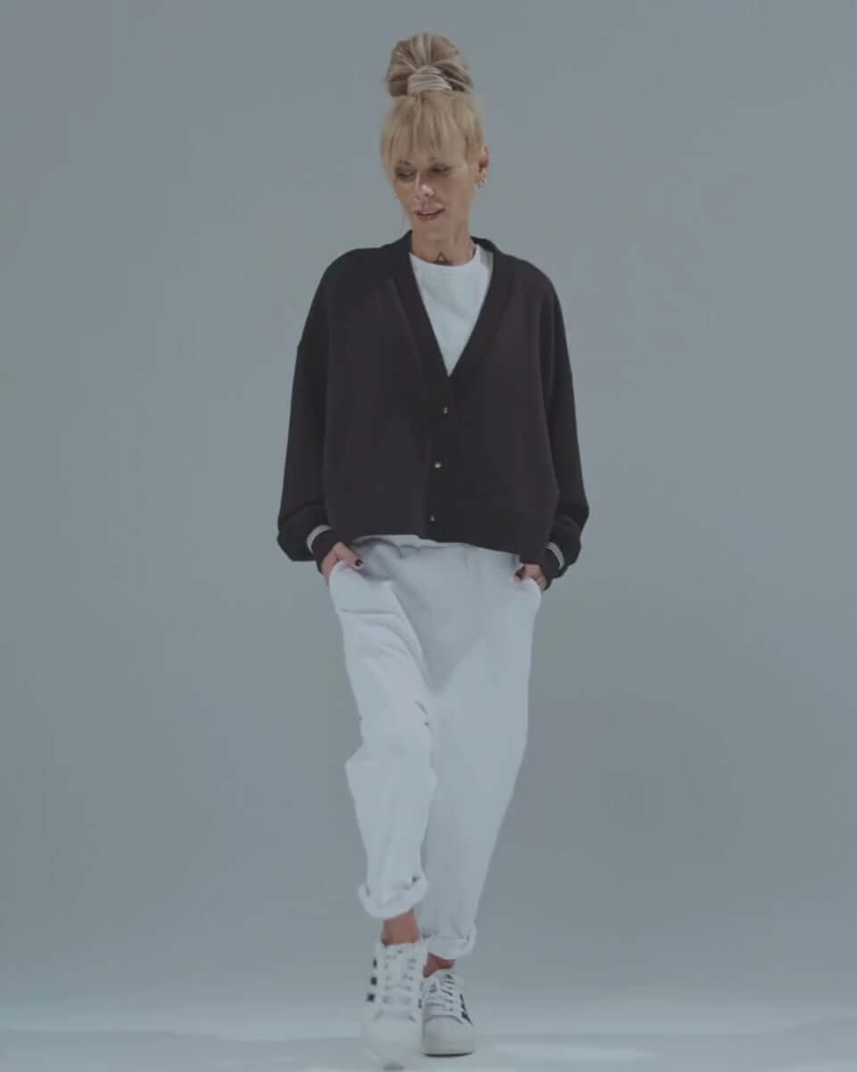 Model wearing a black snap-button jacket paired with white joggers and sneakers, showcasing a relaxed, modern style.