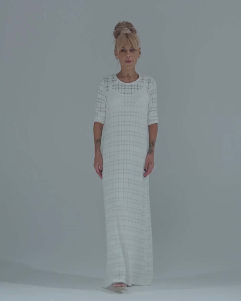 White knitted cotton dress on model, featuring an asymmetrical layered cut and lightweight, semi-sheer fabric.