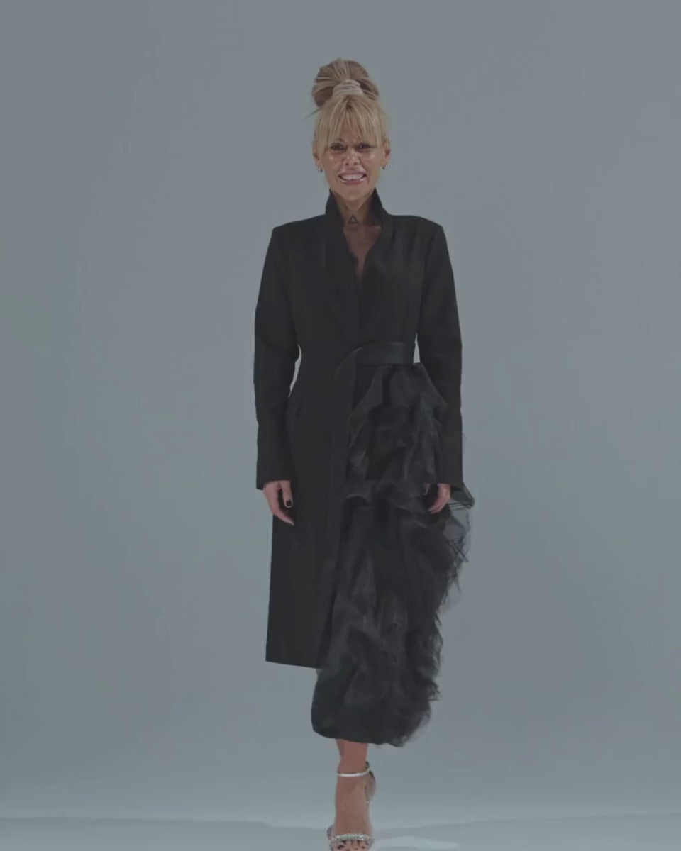 Model showcasing a black tulle detail blazer with a satin waist belt and dramatic asymmetric tulle accent.